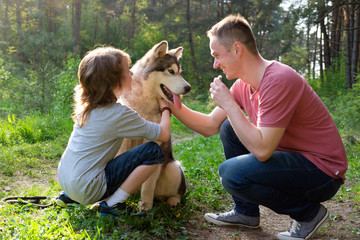 father and  son with their dog malamute on a walk in the forest