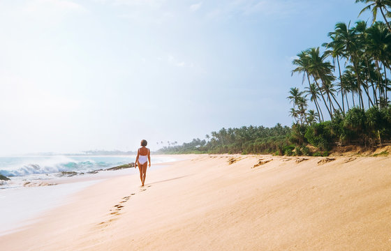 Woman in white swimsuit walks on lonely sand tropical beach