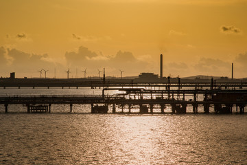 Fototapeta premium Skyline industrial area Cagliari, Sardinia Italy. View from the sea of an oil refinery plant from industry zone with cloudy sky at sunset. Oil storage tank in port area.