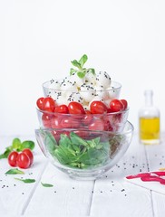 Green salad, cherry tomatoes, mini mozzarella, olive oil. Organic food on a white wooden background. Free space