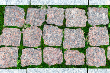 Texture, background of sett blocks different texture. Vintage, Rusty tiled, colorful, decorative granite pavement with green grass and moss.