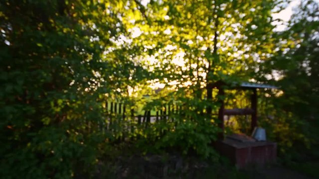 Sunset at old village. Camera flying through the trees to the old well. Steadicam shot.