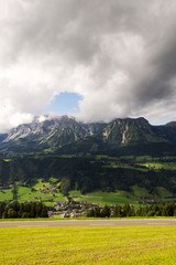 Paraglider flying over Schladming town with Dachstein mountains background, Northern Limestone Alps, Austria, dramatic cloudy sky