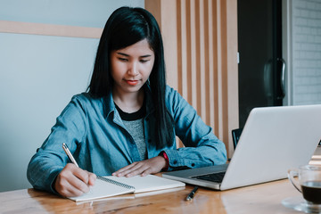 Young business woman sitting at table and writing in notebook