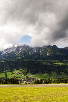 Paraglider flying over Schladming town with Dachstein mountains background, Northern Limestone Alps, Austria, dramatic cloudy sky