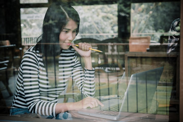 Asian beautiful woman using her laptop and looking laptop screen while Planning thinking concept in cafe.