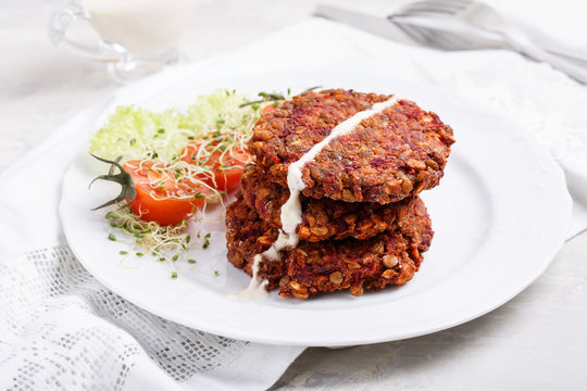 Vegan burgers from lentils, oats and vegetables. Veggie cutlets served with green salad and tomatoes.