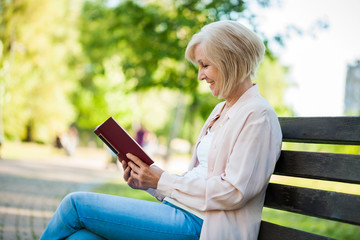 Adult woman sitting in park and reading book.