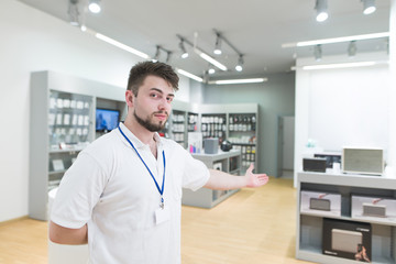 Consultant stands in the bright modern electronics store and invites you with a hand. Portrait of a...