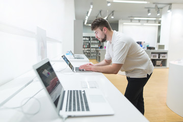 Man uses a laptop in the computer department of the technology store. Showcase with laptops. The...