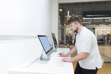 Obraz premium Man uses a computer in a modern electronics store. Buyer selects a monoblock in a light tech store. Buy a computer. Purchase monoblock. Choosing a computer in the store