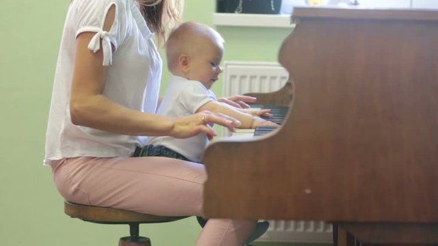 Mother and toddler baby boy, playing piano at home, child learning