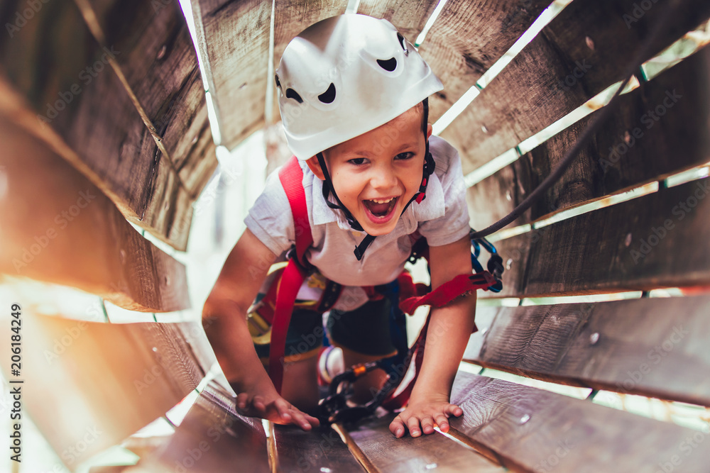 Wall mural little boy climbing in adventure activity park with helmet and safety equipment