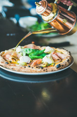 Italian lunch or dinner. Freshly baked pizza with artichokes, smoked turkey ham, olives, cream cheese and basil on table in restaurant, selective focus