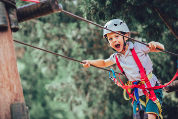 Little boy climbing in adventure activity park with helmet and safety equipment