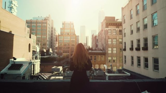 Back View Shot of Beautiful Red Haired Woman Standing on a Roof. Urban Cityscape View of New York City with Great Skyscrapers and Buildings. Shot on RED Epic 4K UHD Camera.