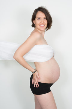 Beauty young pregnant woman with blowing white material in grey background