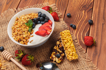 Bowl of homemade granola with yogurt and fresh berries on wooden background