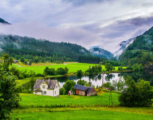 Obraz premium Typical countryside Norwegian landscape with houses on the shore of the lake. Cloudy summer morning in Norway, Europe. Artistic picture. Beauty world.