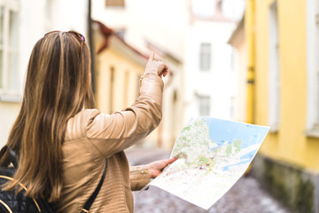 Tourist with map in the city. Woman pointing at right direction with finger. Back view of happy traveler using tourism guide. Person with backpack sightseeing on vacation.