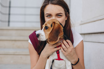 Portrait of beautiful young woman with little beagle puppy sitting outdoors. Woman with blue eyes looking at the camera