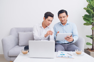 Two confident young businesspeople using a laptop discuss information while sitting on a sofa in a modern office