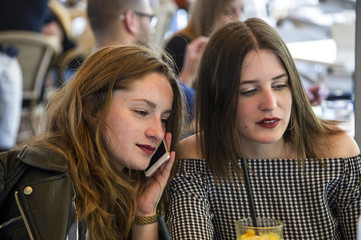 Two young and trendy hipster woman are working in a cafe bar, having an outdoor meeting. Lifestyle conception. 