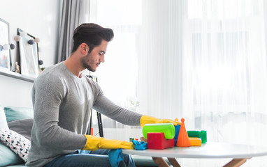 Young handsome father cleaning toys and table after playing with his child at home