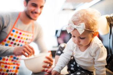 Smiling dad preparing food in the kitchen and takes care of his little daughter, family lifestyle