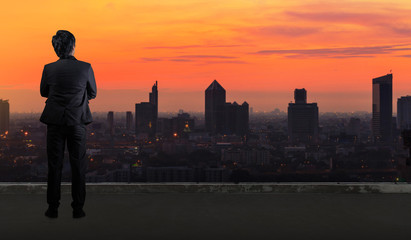 Businessman standing on roof and looking at Cityscape skyline night light