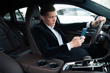 Be careful on the road! Young serious intelligent handsome entrepreneur texting the message, while...