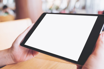 Mockup image of hands holding black tablet pc with blank white desktop screen on wooden table