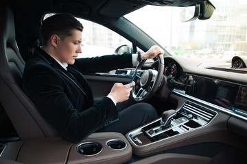 Texting while driving! Side view portrait of the handsome confident young businessman setting his...