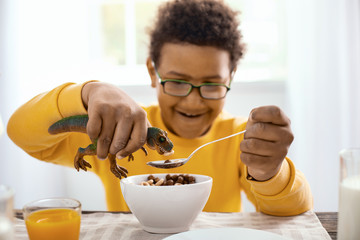 Delicious snack. Pleasant pre-teen boy eating cereals for breakfast and feeding them to his toy...