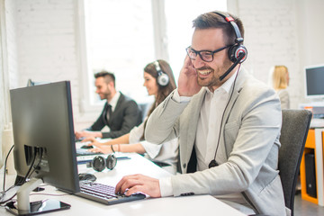 Smiling business man with headset talking with client in call centre