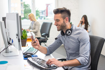 Fototapeta premium Beautiful handsome man call operator with headset around neck using smart phone in office