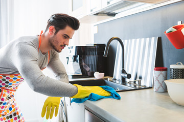 Handsome man in yellow gloves cleaning kitchen, modern masculinity