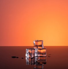 Three ice cubes and water on warm dark orange background