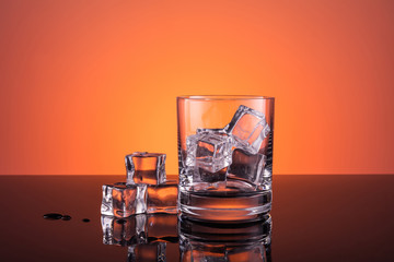 Empty glass with ice prepared for the drink on warm dark orange background