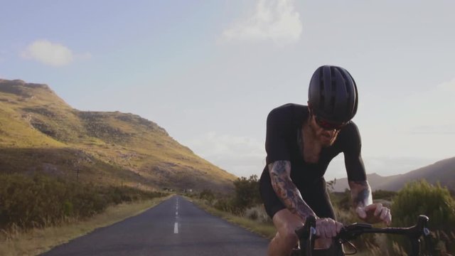 Video shot of male cyclist drinking water and pouring water on his head to stay hydrated during cycling training. Racer rehydrating himself with water while riding a bicycle on open road.