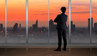 Businessman standing in Office building looking at Cityscape skyline night light