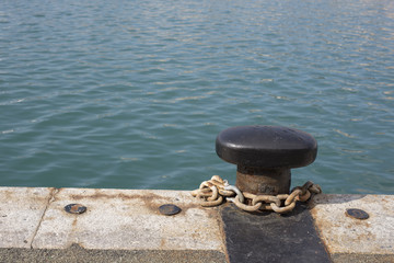 Metal bollard and chain on a stone quay overlooking the sea in a marina or docks