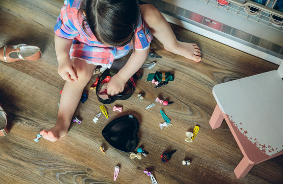 Top view of cute baby girl playing with hair clips collection sitting in a wooden floor at home