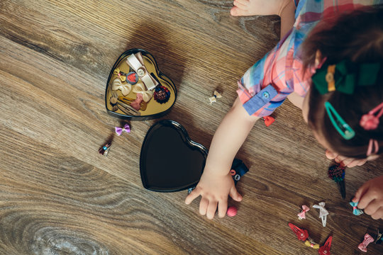 Top view of cute baby girl playing with hair clips collection sitting in a wooden floor at home