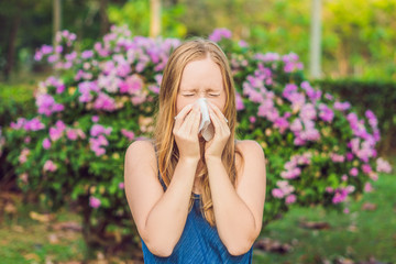Pollen allergy concept. Young woman is going to sneeze. Flowering trees in background