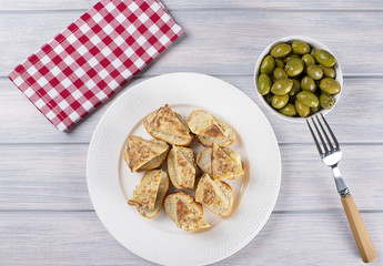 Plate with omelette caps and a fork next to bowl with olives on wooden table. Typical spanish food.