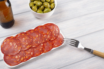 Plate with chorizo next to bowl with olives and cold beer. Food