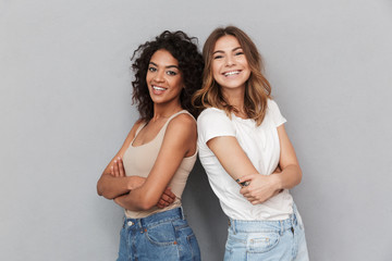 Portrait of two cheerful young women standing together - obrazy, fototapety, plakaty