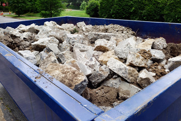 Dumpster filled with sidewalk concrete debris in neighborhood setting.