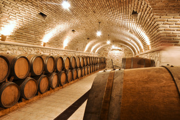 Wine barrels in the old basement of a winery storage. Cellar of restaurant wine vault with brick stone walls.